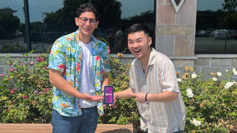 Young entrepreneurs Anthony Nasser and Kevin Le holding a smartphone between them displaying the loading screen for their mobile app Down