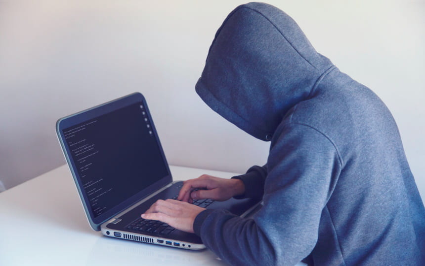 Hooded hacker types on laptop